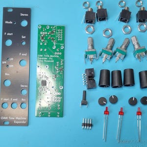 May include: Electronic components laid out on a blue surface. Includes a circuit board labeled "OAM Time Machine Expander," a black metal panel, potentiometers, jacks, and other small parts. The components are for a DIY electronic project.