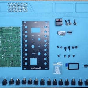 Puede incluir: Un kit de sintetizador electrónico DIY que incluye una placa de circuito verde etiquetada como Timo Rozendal Filler v1.1, un panel frontal negro con texto que incluye Filler, Drummer y Reset, varios potenciómetros, perillas, jacks y componentes.