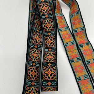 May include: Decorative ribbon with a black background and a repeating floral pattern in shades of orange, yellow, and teal. The ribbon is intricately designed with a detailed, symmetrical motif, suitable for various craft projects.