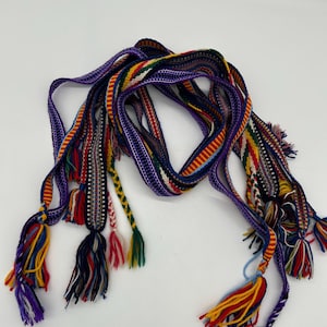 Pu&ograve; includere: Una cintura tessuta colorata con pi&ugrave; fili e nappe decorative. La cintura presenta una vibrante gamma di colori, tra cui viola, rosso, giallo e verde. Le nappe sono fatte di pi&ugrave; fili di filo.