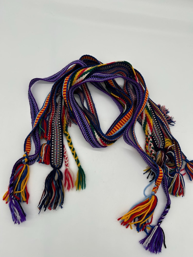 Pu&ograve; includere: Una cintura tessuta colorata con pi&ugrave; fili e nappe decorative. La cintura presenta una vibrante gamma di colori, tra cui viola, rosso, giallo e verde. Le nappe sono fatte di pi&ugrave; fili di filo.