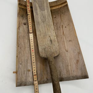 May include: A rustic wooden butter paddle and a wooden butter board. The paddle is approximately 38 cm long. The board is rectangular with a curved edge. The wood has a weathered appearance, with visible grain and knots.