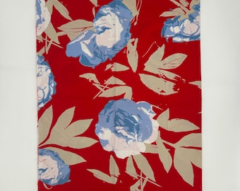 May include: A red fabric with a floral pattern featuring large blue and white flowers and tan leaves. The fabric has a bold, eye-catching design, perfect for home decor or apparel projects. The fabric is labeled "TÄYSIIKU" 100% CO.