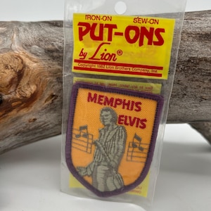 May include: A vintage "Memphis Elvis" iron-on patch in a clear plastic package. The patch is orange with a purple border and features an illustration of Elvis Presley. The packaging reads "PUT-ONS by Lion" in red and yellow.