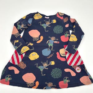 May include: Navy blue long-sleeve dress with a whimsical pattern of cartoon figures, abstract shapes, and dots in various colors. The dress features red and gray striped accents and a small logo patch.