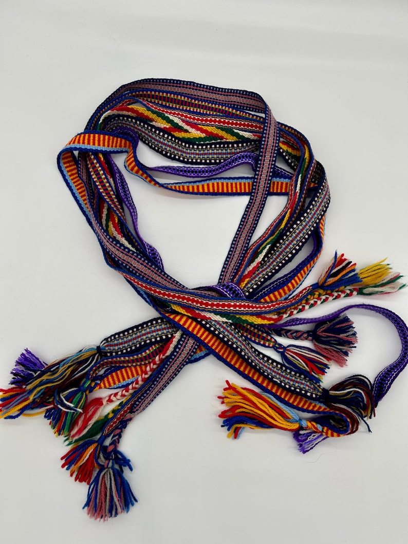 Pu&ograve; includere: Una cintura intrecciata multicolore con nappe. La cintura presenta diversi fili di vari colori, tra cui rosso, giallo, blu e viola. Le nappe sono attaccate alle estremit&agrave;. Probabilmente fatto a mano.