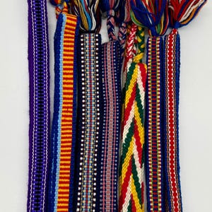 Pu&ograve; includere: Una collezione di cinghie tessili colorate intrecciate con nappe intrecciate. Le cinghie presentano vari modelli e combinazioni di colori, tra cui blu, rosso, giallo e bianco. Queste cinghie decorative sono probabilmente utilizzate per abbellire o creare.