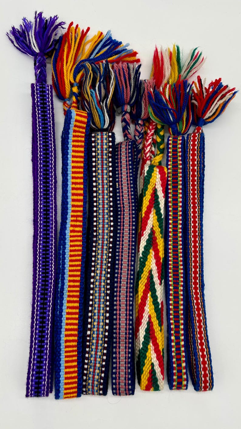 Pu&ograve; includere: Una collezione di cinghie tessili colorate intrecciate con nappe intrecciate. Le cinghie presentano vari modelli e combinazioni di colori, tra cui blu, rosso, giallo e bianco. Queste cinghie decorative sono probabilmente utilizzate per abbellire o creare.