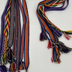 Pu&ograve; includere: Una collezione di cinture tessute colorate con nappe. Le cinture presentano vari motivi e colori, tra cui rosso, blu, giallo e viola. Ogni cintura ha un design unico ed &egrave; rifinita con una nappa.