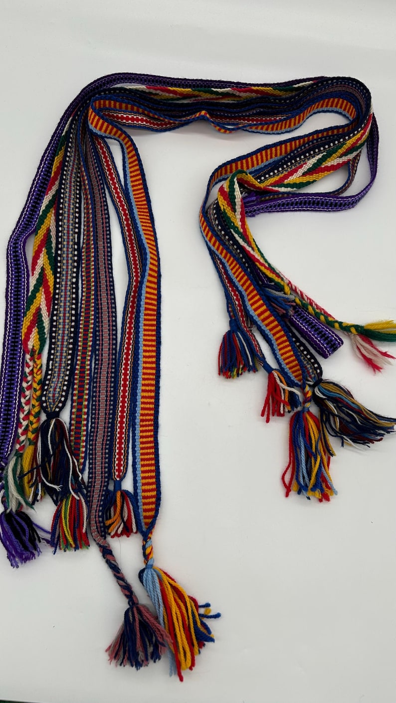 Pu&ograve; includere: Una collezione di cinture tessute colorate con nappe. Le cinture presentano vari motivi e colori, tra cui rosso, blu, giallo e viola. Ogni cintura ha un design unico ed &egrave; rifinita con una nappa.