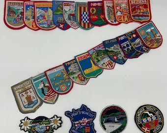 Może przedstawiać: Kolekcja haftowanych naszywek z różnymi wzorami miast i regionów europejskich. Naszywki przedstawiają kolorowe ilustracje zabytków, herbów i lokalnych scen. Naszywki są w różnych kształtach i rozmiarach, z czerwonymi obramowaniami.