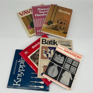 Op de afbeelding: Een verzameling vintage handwerkboeken met titels als "Vävning" en "Batik". De boeken hebben kleurrijke covers met illustraties van weven, breien en andere textielambachten. De boeken zijn op een wit oppervlak gestapeld.