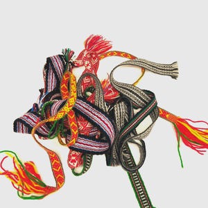 May include: A collection of woven fabric bands featuring intricate geometric patterns in vibrant colors including red, yellow, green, black, and white. These narrow, decorative textile strips are intertwined, with some ends finished with loose, multi-colored yarn tassels.
