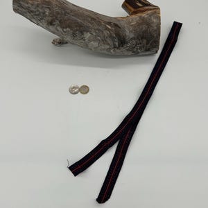 May include: A piece of driftwood with a textured, grey and brown surface. A black and red patterned ribbon lies next to the wood. Two coins are also present.