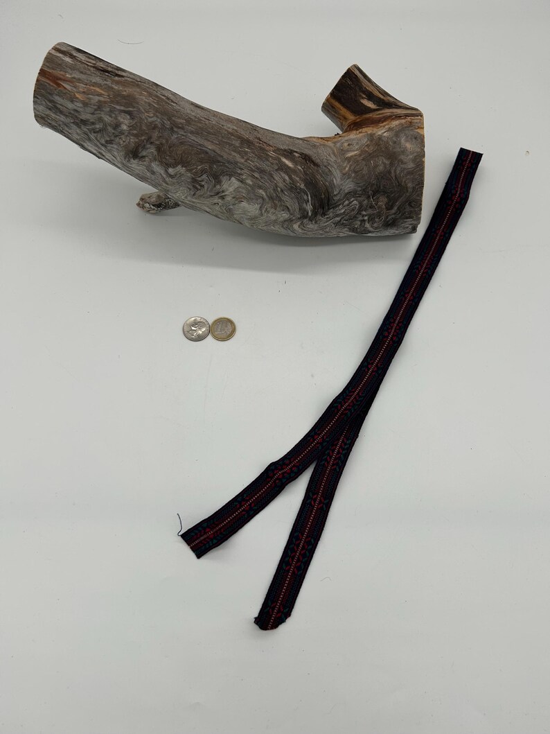 May include: A piece of driftwood with a textured, grey and brown surface. A black and red patterned ribbon lies next to the wood. Two coins are also present.