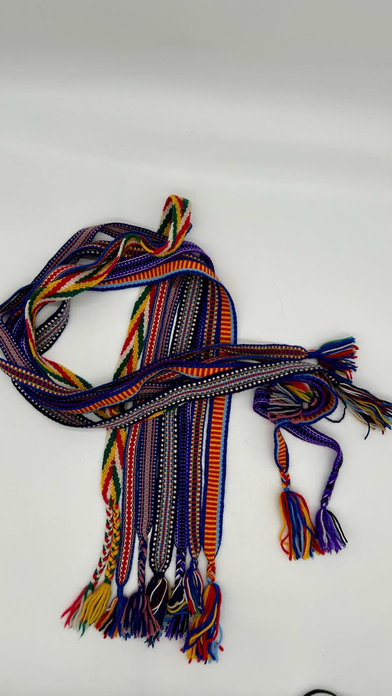 Pu&ograve; includere: Una collezione di nastri colorati tessuti con motivi intricati e nappe. I nastri presentano una variet&agrave; di colori, tra cui rosso, giallo, blu e verde, e sono probabilmente utilizzati per scopi decorativi o artigianali.