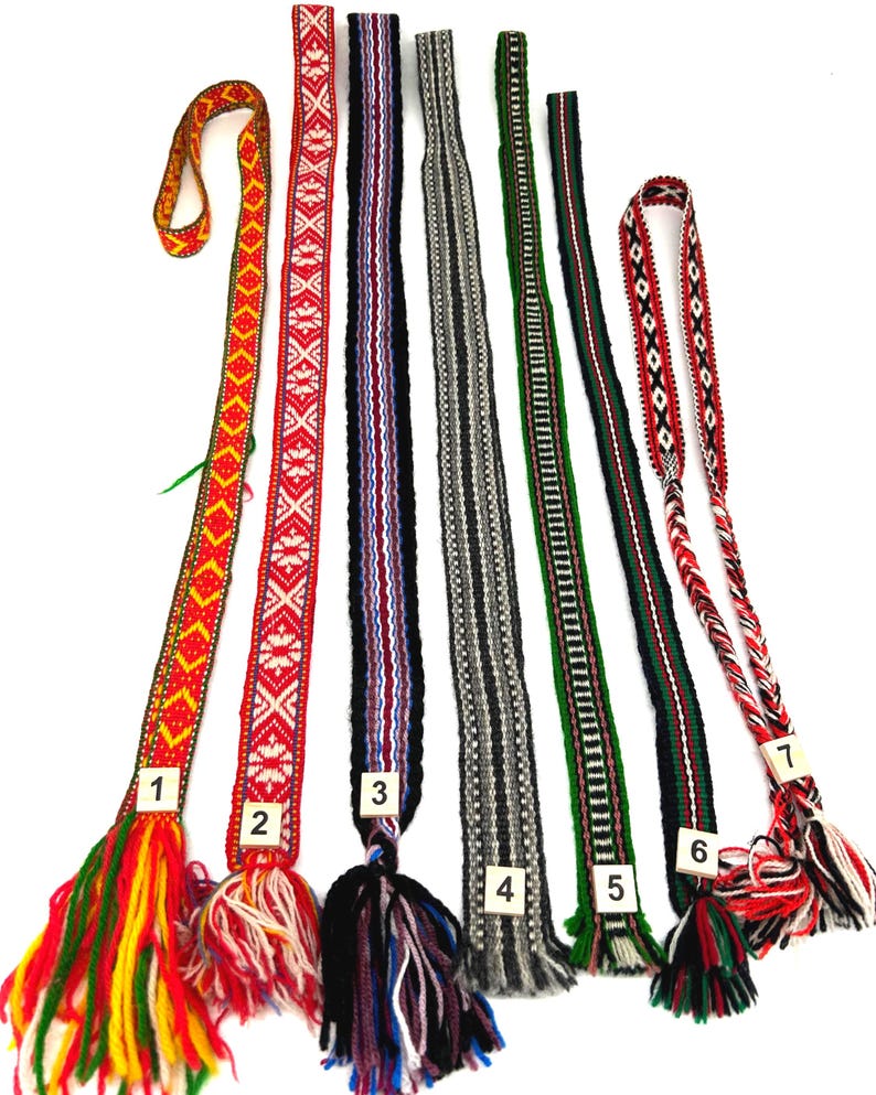 May include: Seven long, narrow woven fabric belts or sashes, each featuring distinct geometric patterns and color combinations, including red, yellow, green, black, white, and grey, with numbered tags and fringed ends at the bottom of each.