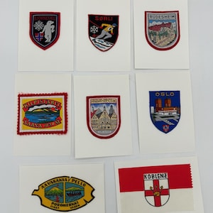 May include: A collection of embroidered patches featuring various city and landscape designs. The patches are rectangular and shield-shaped, with vibrant colors and detailed imagery, including text such as "Oslo" and "Frankfurt/M".
