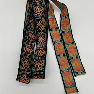 May include: Two decorative ribbons with intricate floral and geometric patterns. The ribbons feature a black background with orange, yellow, and teal accents. The ribbons are likely used for embellishment or crafting.