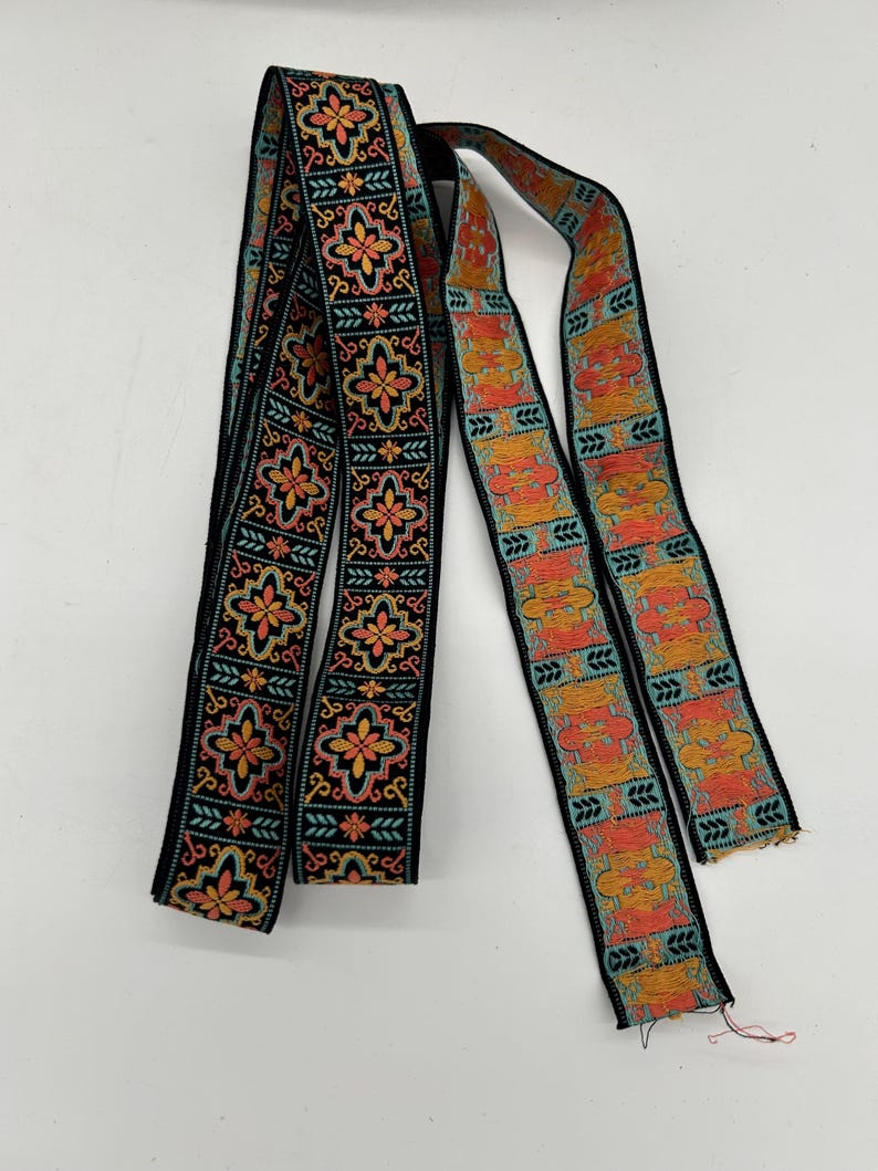May include: Two decorative ribbons with intricate floral and geometric patterns. The ribbons feature a black background with orange, yellow, and teal accents. The ribbons are likely used for embellishment or crafting.