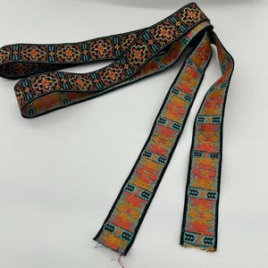 May include: A length of decorative ribbon with a black background and a repeating pattern of orange and teal floral and geometric designs. The ribbon is likely used for crafting or embellishment.