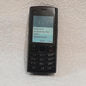 May include: A black Nokia X2 cell phone with a screen displaying Russian text. The phone has a keypad with numbered buttons and a navigation pad. The screen shows a prompt asking to start the device without SIM1.