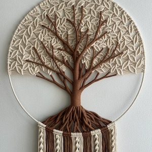 May include: A circular macrame wall hanging featuring a brown cord tree with intricate roots and branches. The canopy is crafted from cream-colored cord in a leaf-like pattern. Below the tree, vertical cream and brown cords hang in rows.