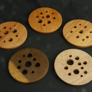 Op de afbeelding: Vijf ronde houten onderzetters met een cirkelvormig patroon van gaten in het midden. De onderzetters zijn gemaakt van verschillende soorten hout, waaronder licht en donker hout.