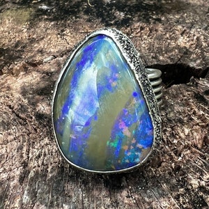 May include: A silver ring with a large, teardrop-shaped opal gemstone. The opal is a mix of blue, green, and white.