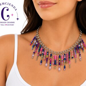May include: A silver-toned chain necklace featuring a fringe of dangling beads in various colors including pink, purple, blue, and green. The necklace is displayed against a white background with a logo in the corner reading Charmcienda.