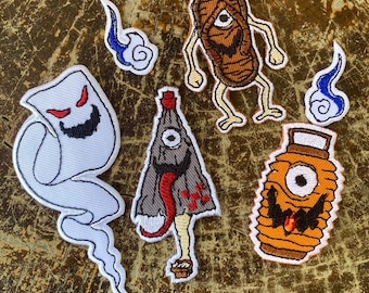 Puede incluir: Un conjunto de parches bordados con diseños de Halloween. Incluye un fantasma blanco con una cara roja, una momia con un ojo, una linterna, una criatura con una lengua roja y dos diseños de llamas azules y blancas.