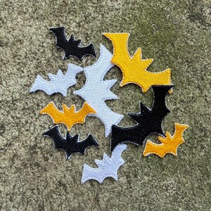 May include: A group of embroidered bat patches in black, white, and yellow. The patches are in different sizes and arranged together. The bats have a stitched outline, suitable for crafting or decorating Halloween-themed items.