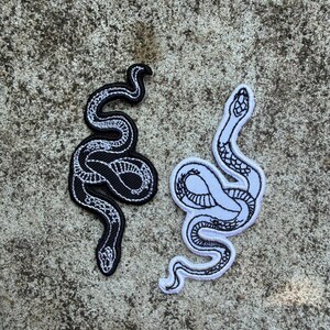 May include: Two embroidered snake patches. One is black with white detailing, the other is white with black detailing. Both patches feature a detailed snake design with a curved, sinuous form.