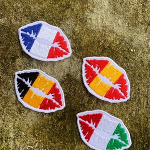 May include: Four embroidered patches in the shape of lips, each with a unique design. One features blue and red, another black, yellow, and red, a third yellow and red, and the last red and green. All have a white center and white border.