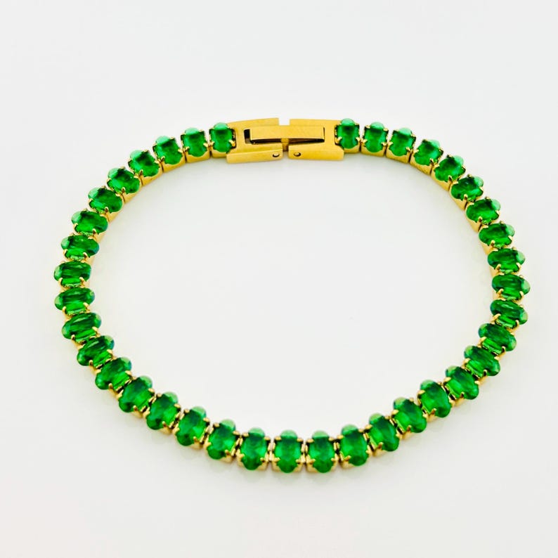 K&ouml;nnte beinhalten: Ein goldenes Tennisarmband mit gr&uuml;nen ovalen Steinen.
