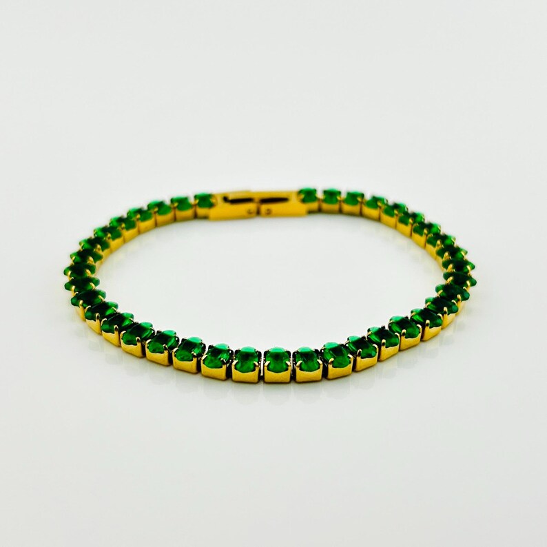K&ouml;nnte beinhalten: Ein goldenes Armband mit einer Reihe von smaragdgr&uuml;nen Steinen.