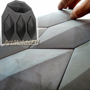 Puede incluir: Un molde de silicona negro con cuatro impresiones en forma de diamante. El molde se utiliza para crear baldosas de hormigón con un patrón geométrico. Las baldosas terminadas se muestran en el fondo.