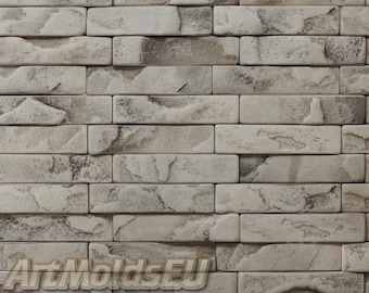 May include: A close-up of a wall made of gray and white brick-shaped tiles. The tiles have a rough, textured surface that resembles stone.