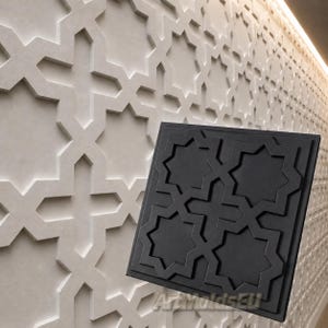 Op de afbeelding: Een zwart decoratief paneel met een geometrisch sterpatroon, afgebeeld tegen een muur met een vergelijkbaar, maar lichter, textuurontwerp. Het paneel is vierkant en heeft een herhalend achtpuntig stermotief. De muur heeft een herhalend patroon.