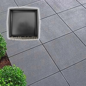 May include: A square, black paving stone mould with rounded corners and a raised edge. The image is set on a grey tiled surface, with a small green bush in the lower left corner. The text "ArtMoldsEU" is visible.