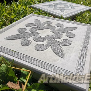 May include: A square concrete stepping stone with a decorative grey floral design. The stone has a textured border.