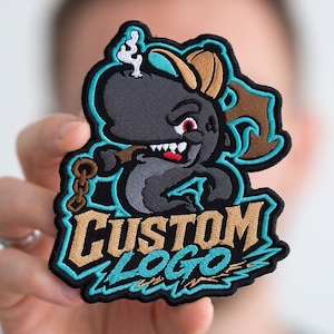 May include: An embroidered patch featuring a cartoon shark wearing a tan cap, smoking a cigar, and holding a chain. The shark is gray with red eyes and white teeth. Below the shark, the text CUSTOM LOGO is stitched in tan and bright blue thread.
