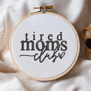 Peut inclure: Cerceau brod&eacute; avec le texte "tired moms club" en lettres noires et un petit c&oelig;ur.