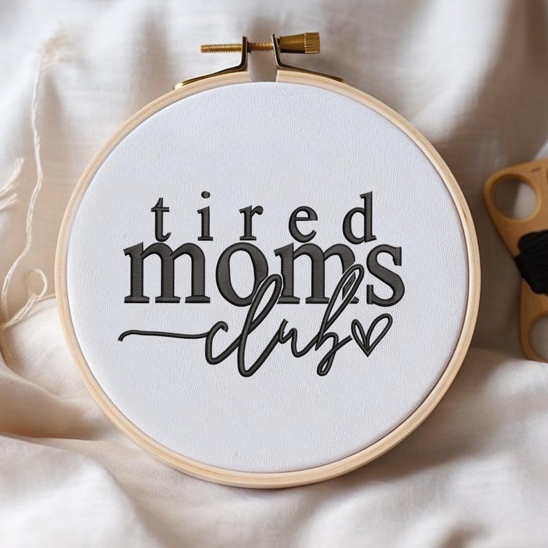 Peut inclure: Cerceau brod&eacute; avec le texte "tired moms club" en lettres noires et un petit c&oelig;ur.