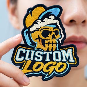 May include: An embroidered patch featuring a yellow skull wearing a light blue and yellow baseball cap, with the text CUSTOM LOGO in light blue and yellow block letters below the skull, all outlined in a thick dark navy blue border.