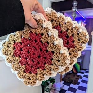 May include: Two crocheted granny squares in brown, red, and white. The squares are joined together and have a scalloped edge.