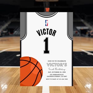 May include: A basketball-themed invitation featuring a jersey design with the name "Victor" and the number "1". An orange basketball graphic is on the left. The invitation includes event details: "Victor's First Birthday" on October 20th.
