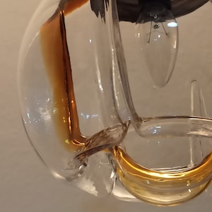Op de afbeelding: Een hanglamp van helder glas met een gouden binnenkant. De lamp heeft een unieke, organische vorm.