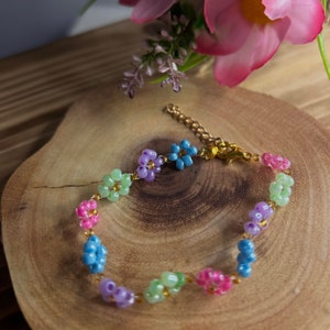 May include: A colorful beaded bracelet with flower-shaped charms in shades of green, purple, pink, and blue. The bracelet is made with small beads and has a gold clasp.