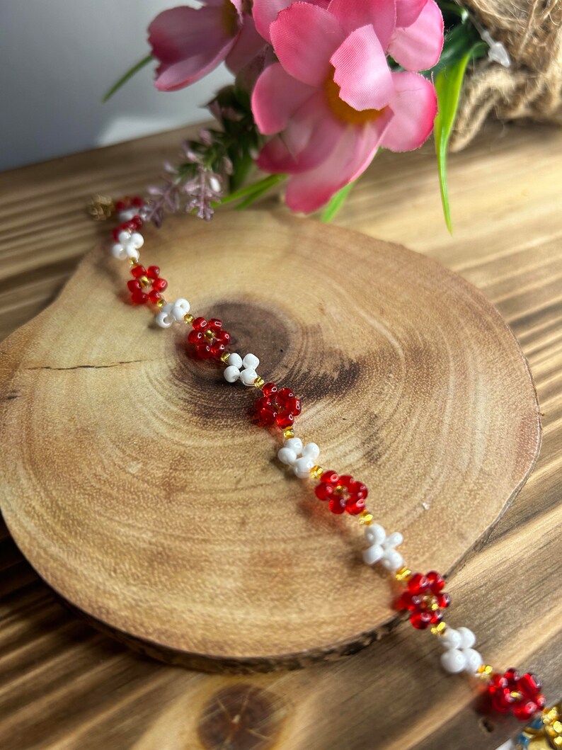 May include: A red and white beaded bracelet with flower-shaped beads. The bracelet is on a wooden surface.